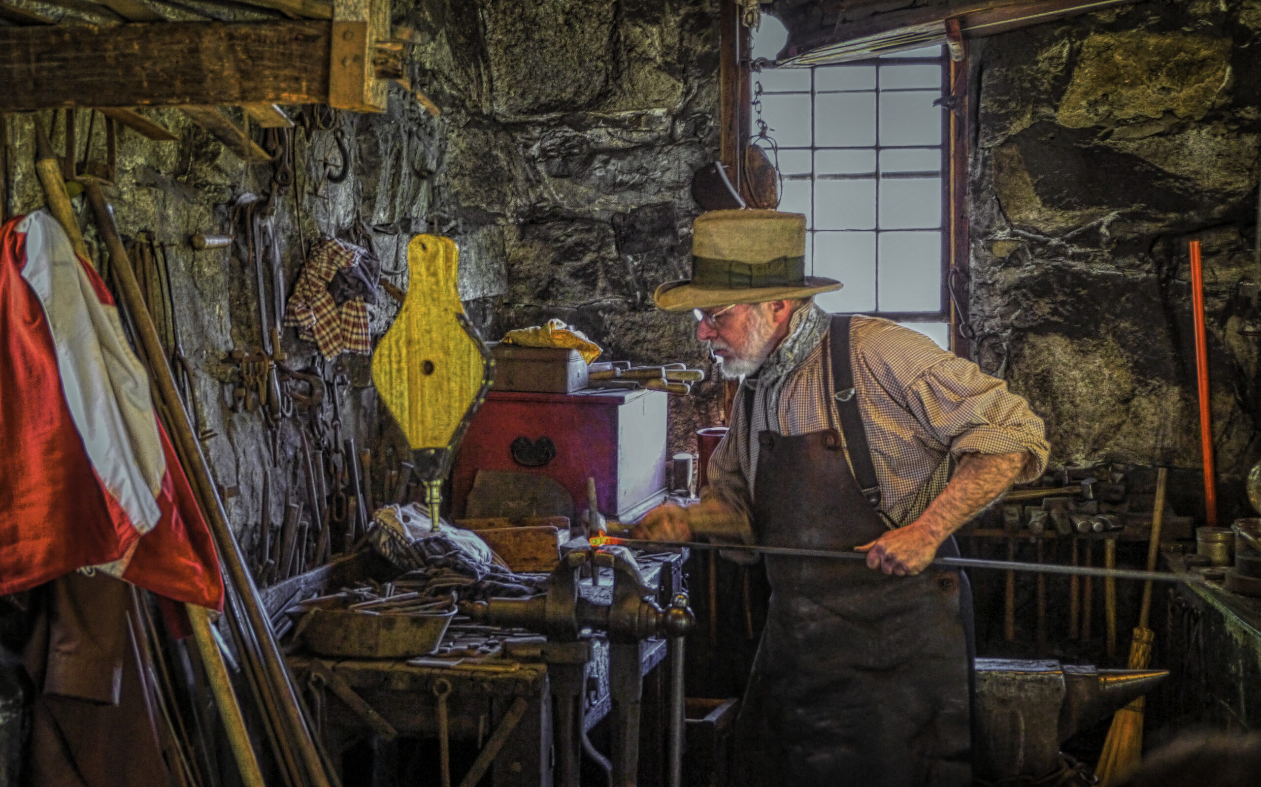 Bearded blacksmith working on a piece of metal at Sturbridge, Massachusetts