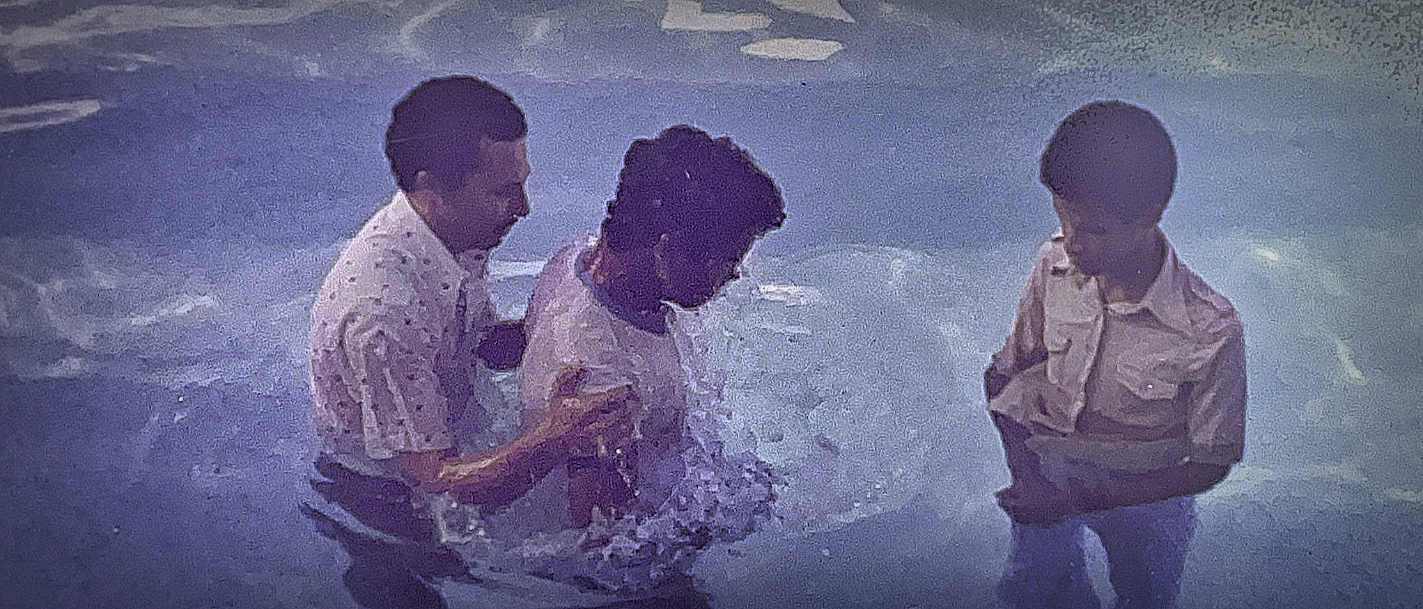Pastor baptizing a young man as another young man watches