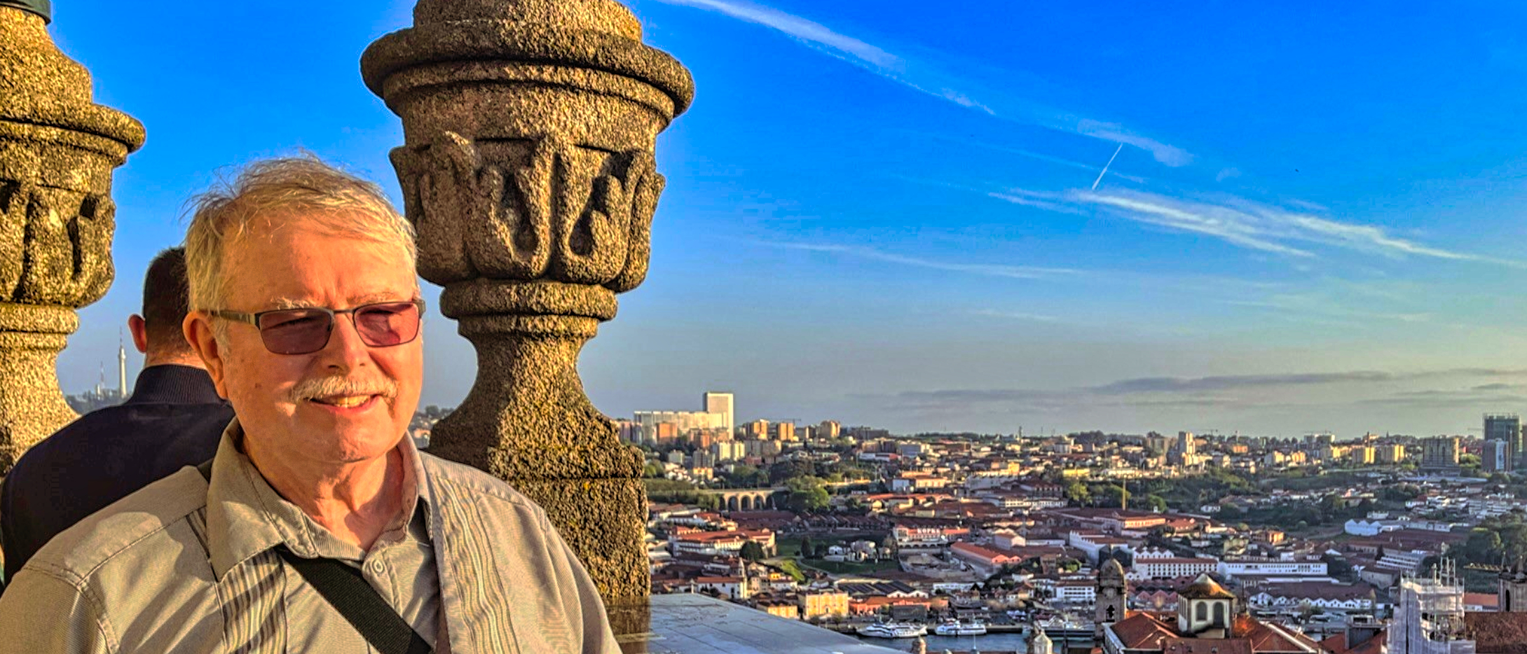 A man with glasses smiling with the city of Porto, Portugal behind him