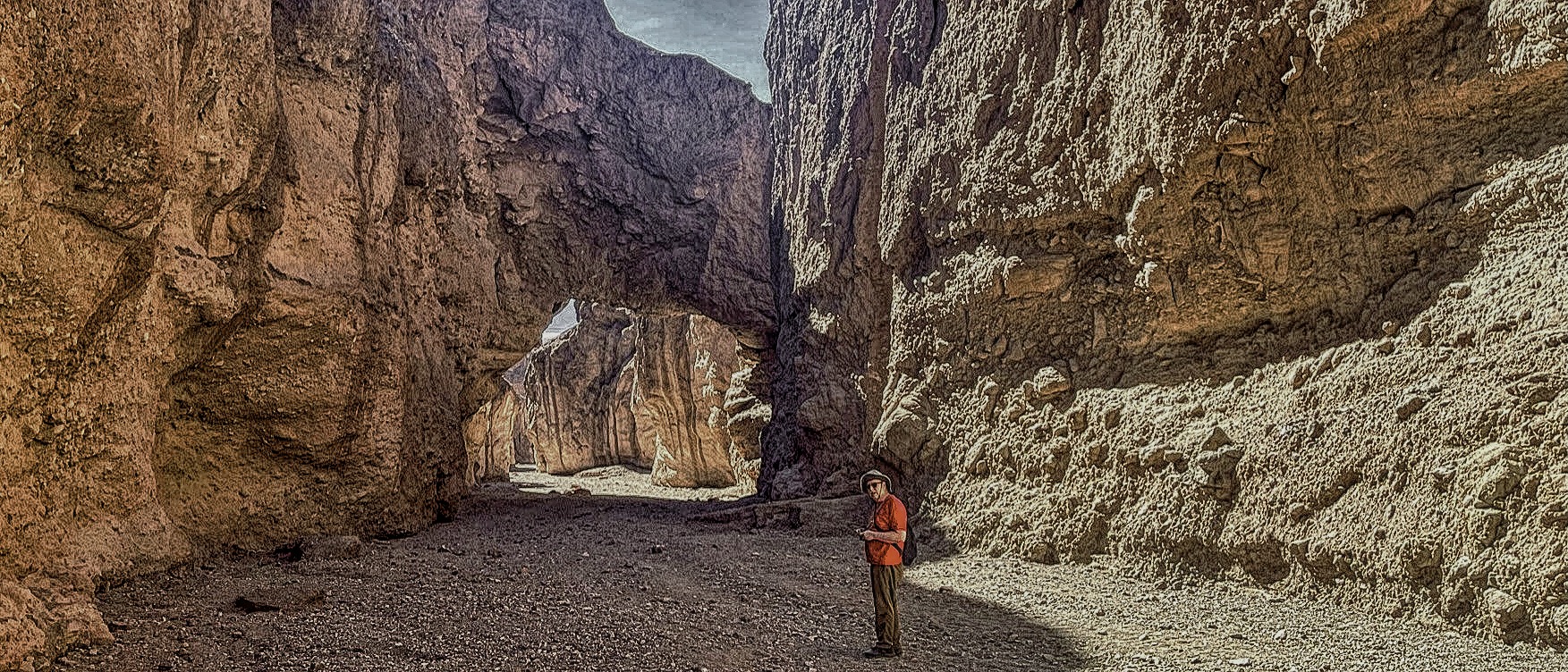 Man in red shirt standing near a natural rock bridge in Death Valley, California